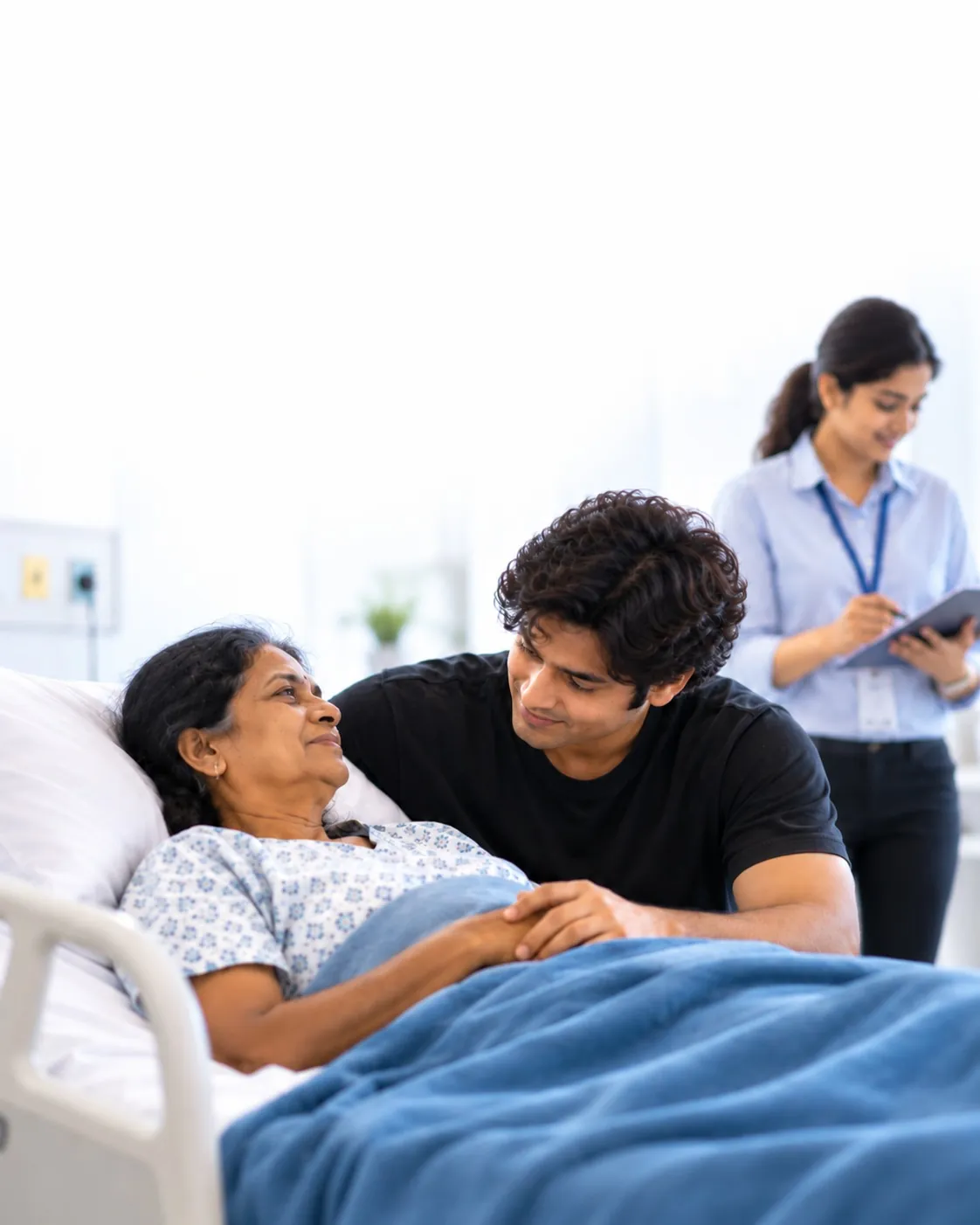 A son holding his mother's hand in her hospital bed while the care coordinator completes the admission